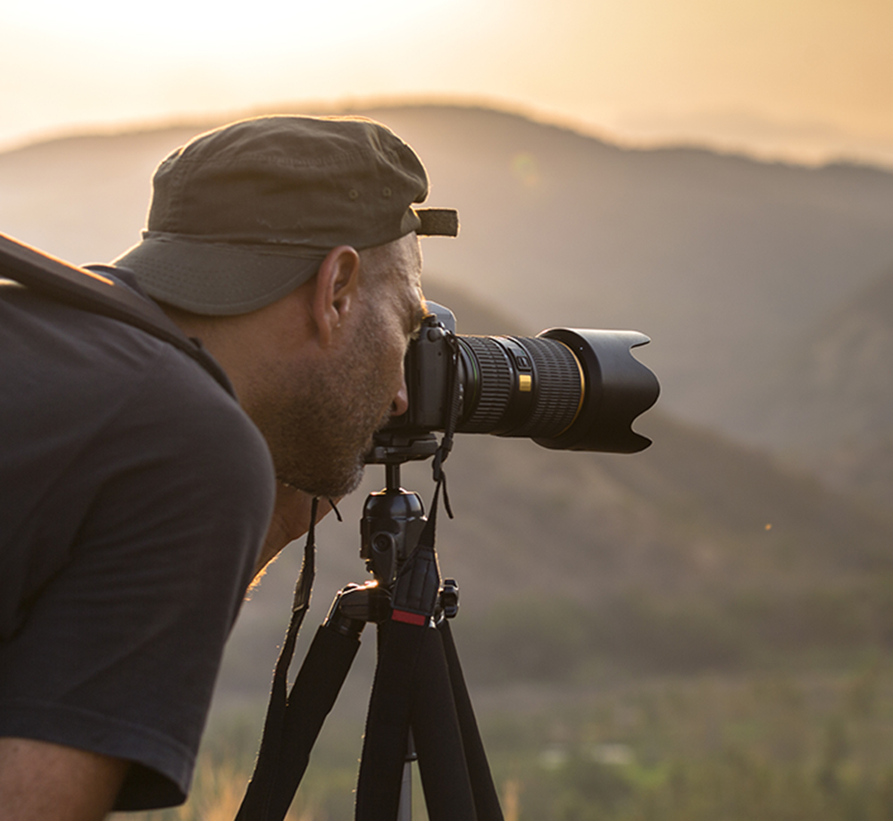 Fotograf fotografiert mit einer Kamera auf einem Stativ eine Berglandschaft im warmen Sonnenlicht